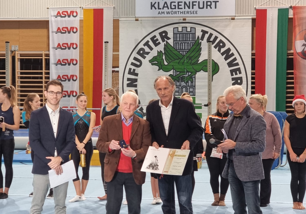 v.l.n.r. Robin Wadl; Langzeitobmann und Geehrter Siegfried Legner; ASVÖ-Kärnten-Präsident Dr. Christoph Schasché; der neue Obmann DI Reinhold Luschin; im Hintergrund die Turner:innen des KTV | © ASVÖ Kärnten/CS